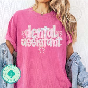 K&ouml;nnte beinhalten: Ein pinkfarbenes T-Shirt mit dem Schriftzug "dental assistant" in dekorativer Schrift. Der Text ist wei&szlig; und hellblau, mit floralen und Schleifen-Akzenten. Das Shirt hat eine einfarbige pinke Farbe.