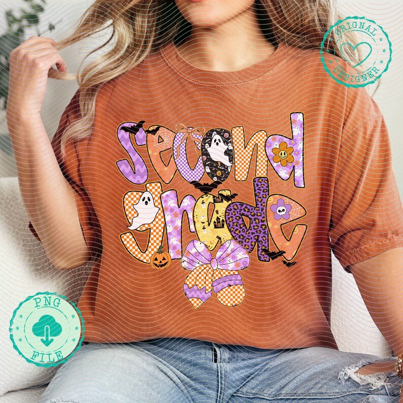 K&ouml;nnte beinhalten: Gebrannt orangefarbenes T-Shirt mit einem farbenfrohen "Second Grade"-Aufdruck. Das Design zeigt Geister, Flederm&auml;use, einen K&uuml;rbis und eine Schleife. Der Text ist in verschiedenen Mustern und Farben gehalten, darunter Lila, Orange und Gelb. Ein lustiges, festliches Shirt f&uuml;r das Schuljahr.