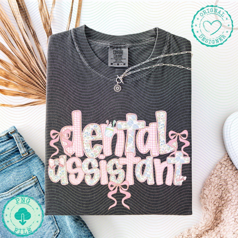 K&ouml;nnte beinhalten: Ein dunkelgraues T-Shirt mit dem Schriftzug "dental assistant" in einem rosa und floralen Design. Das Shirt hat ein wellenf&ouml;rmiges Muster und ist mit einer silbernen Halskette versehen. Ein PNG-Dateilogo befindet sich in der unteren linken Ecke.