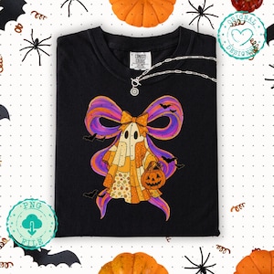 May include: Black t-shirt with a Halloween ghost design. The ghost is wearing a patchwork outfit and holding a jack-o'-lantern. The ghost has a large purple and orange bow. A silver necklace is draped across the shirt.