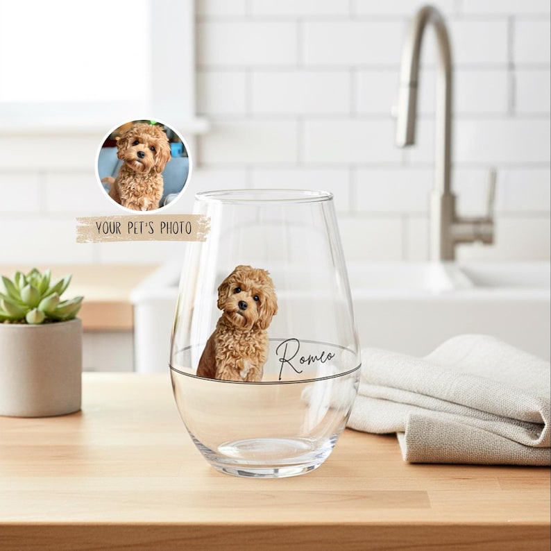 May include: A clear stemless wine glass featuring a custom pet photo and the name "Romeo" in black script. The glass has a water line and a small image of a brown dog inside. The text "YOUR PET'S PHOTO" is above the glass.