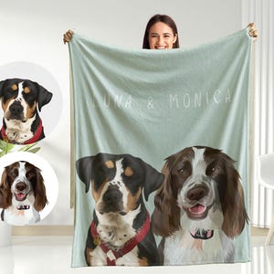 May include: A soft, light blue fleece blanket with the names "Luna & Monica" printed on it. Two dog portraits are featured on the blanket, one of a black and white dog and one of a brown and white dog.