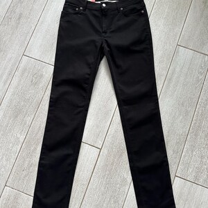 May include: A pair of solid black denim jeans featuring a classic five-pocket design with metal rivets and a button fly closure. The waistband includes a pink and blue brand label that reads Acne Studios, showcasing a slim-fit silhouette.