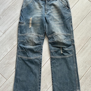 May include: A pair of blue denim jeans with distressed details and reinforced knee patches. The jeans have a relaxed fit and a straight leg.