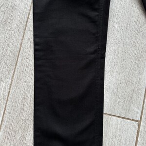 May include: A pair of solid black pants featuring a straight leg cut with visible vertical stitching along the side seam. The fabric has a smooth, matte texture and a consistent deep black color throughout the entire visible length of the garment.