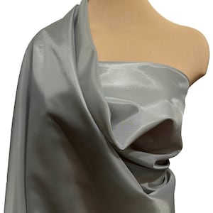May include: A silver taffeta fabric draped over a dress form. The fabric has a subtle sheen and a smooth texture.