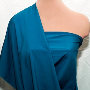 Op de afbeelding: Turkoois stof gedrapeerd over een mannequin. De stof is glad en heeft een lichte glans.