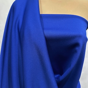 Op de afbeelding: Koninklijk blauwe stof met een glad, licht getextureerd oppervlak. De stof is gedrapeerd over de schouder van een mannequin, waardoor de drape en flow zichtbaar worden.