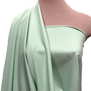 May include: A light green fabric swatch draped over a mannequin. The fabric has a smooth, silky texture.