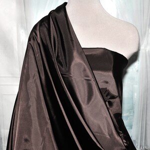 May include: A brown satin fabric draped over a mannequin. The fabric has a smooth, silky texture and a rich, deep brown color.