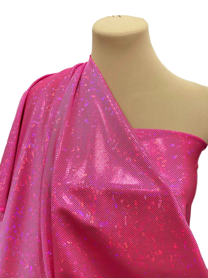 May include: Pink iridescent fabric with a grid pattern. The fabric is shiny and has a holographic effect.