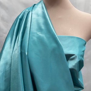 May include: A teal blue satin fabric draped over a dress form. The fabric has a subtle sheen and is smooth to the touch.