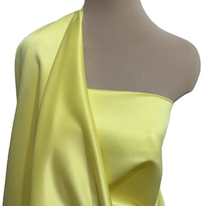 May include: A bright yellow satin fabric draped over a mannequin. The fabric is smooth and silky.