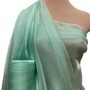 May include: A light green sheer fabric with a shimmery finish. The fabric is draped over a mannequin's shoulder.