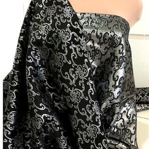 May include: Black fabric with a silver floral pattern. The fabric is woven with a raised design, giving it a textured look.