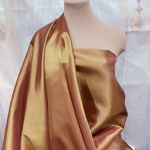 May include: A gold and rose gold taffeta fabric with a subtle sheen. The fabric is draped over a dress form.