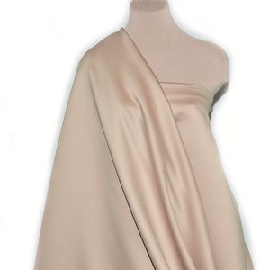 May include: A close-up of a light beige fabric draped over a dress form. The fabric has a smooth, satin-like finish.