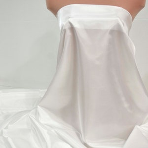 May include: White satin fabric draped over a dress form. The fabric is smooth and silky, with a slight sheen.