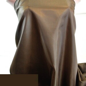 May include: A brown satin fabric with a smooth, silky texture. The fabric is draped over a mannequin, showcasing its luxurious feel.