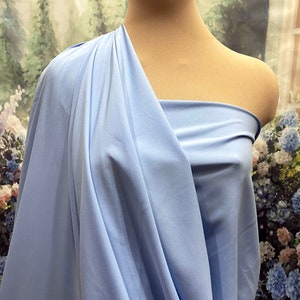 May include: A light blue fabric draped over a mannequin. The fabric is smooth and has a slight sheen. The background is a blurred image of a floral pattern.