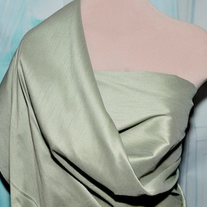 May include: A sage green silk fabric draped over a mannequin. The fabric has a subtle sheen and a smooth texture.