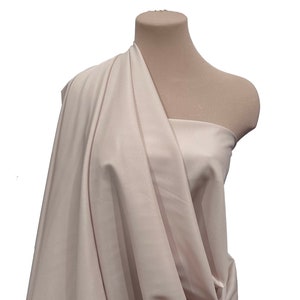 Puede incluir: Primer plano de una tela beige claro drapeada sobre un maniquí. La tela tiene un brillo sutil y una textura suave.