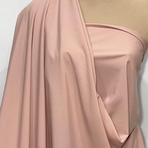 May include: A soft, smooth, blush pink fabric draped over a mannequin. The fabric has a subtle sheen and a slightly textured surface.