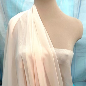 Può includere: Un tessuto leggero e fluido di colore avorio drappeggiato su un manichino. Il tessuto è leggero e ha una texture morbida e fluida.