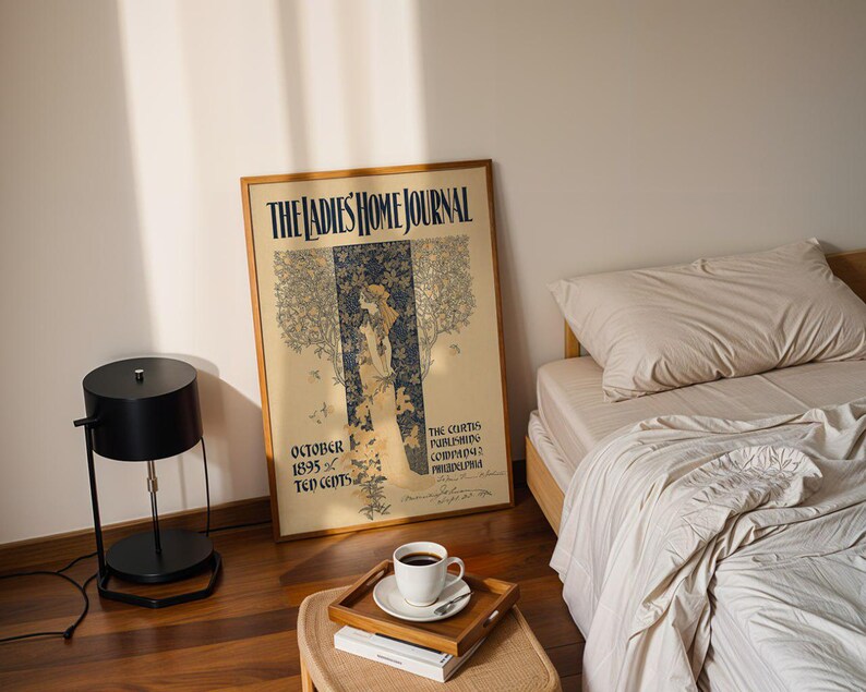 K&ouml;nnte beinhalten: Ein gerahmter Vintage-Druck des Magazins "The Ladies Home Journal" vom Oktober 1895. Der Druck zeigt eine Frau in einem Kleid mit floralem und Baumdesign. Eine schwarze Lampe, eine Tasse Kaffee und ein Bett sind ebenfalls im Bild.
