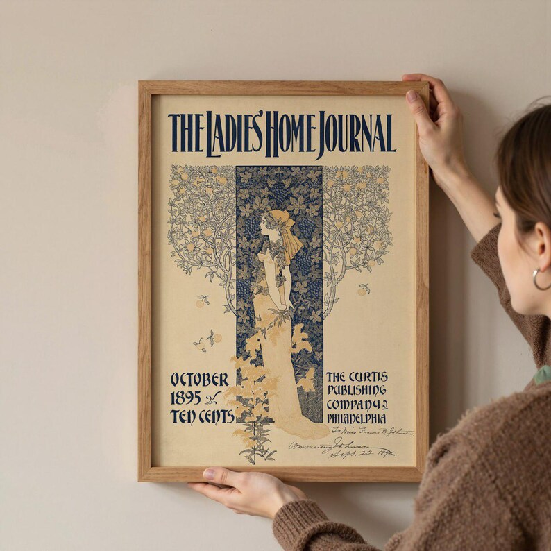 K&ouml;nnte beinhalten: Ein gerahmter Vintage-Druck des Titelblatts der Zeitschrift "The Ladies' Home Journal". Das Kunstwerk zeigt eine Frau in einem flie&szlig;enden Kleid, umgeben von floralen und Rankenmotiven. Der Text enth&auml;lt "Oktober 1895" und "Ten Cents".