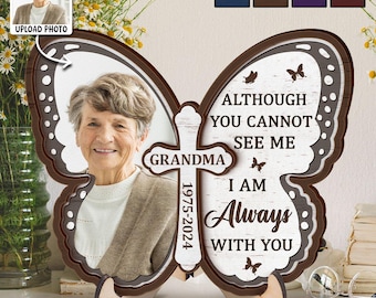 May include: A butterfly-shaped wooden memorial plaque with a photo of a woman. The plaque includes the text "Grandma 1975-2024" and the message "Although you cannot see me, I am always with you."