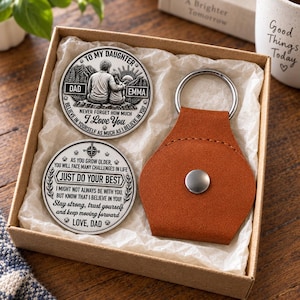 Op de afbeelding: Een geschenkset in een kartonnen doos met twee ronde zilverkleurige metalen munten met gegraveerde tekst en een bruine sleutelhanger in lederlook met een zilveren metalen ring en een drukknoopsluiting. De munten tonen afbeeldingen van ouder en kind.