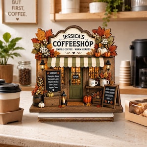 May include: A wooden miniature coffee shop display titled Jessica's Coffeeshop, featuring a green door, striped awning, and autumn-themed decor including orange leaves, white berries, and pumpkins. The sign reads Simple Coffee - Warm Hearts.