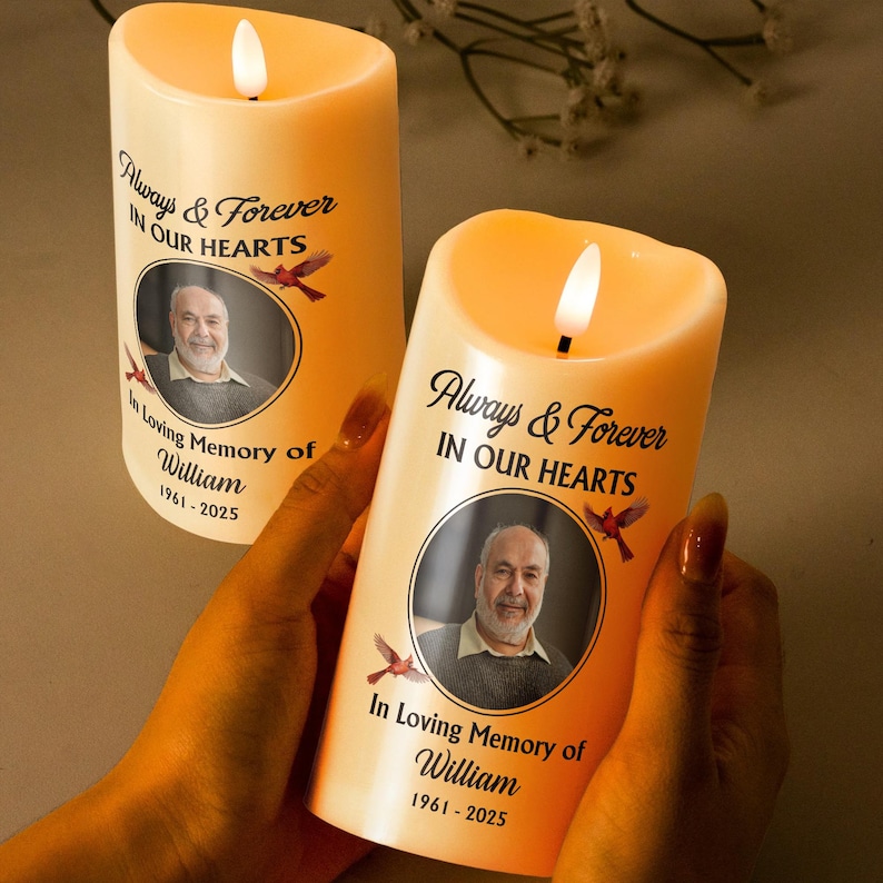Puede incluir: Dos velas LED de color marfil con una llama parpadeante. Cada vela presenta una foto y el texto "Always & Forever IN OUR HEARTS" y "In Loving Memory of William 1961-2025".