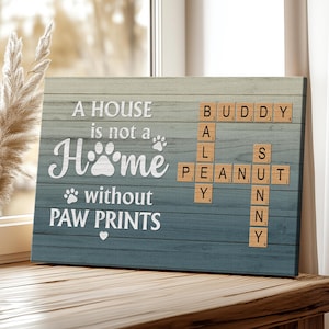 Può includere: Un cartello di legno con uno sfondo sfumato blu e grigio. Il cartello recita "A HOUSE is not a HOME without PAW PRINTS" in scrittura bianca. Tessere di Scrabble compongono "BUDDY, AL, PEANUT, SNY".