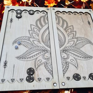 Può includere: Un tabellone di backgammon in legno con un grande disegno floreale inciso al centro. Il tabellone è di colore chiaro con dettagli incisi scuri. Dadi e pedine sono visibili. Il tabellone è circondato da foglie autunnali.