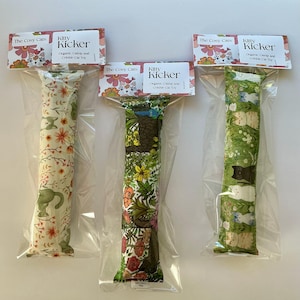 May include: Three cat toys in clear plastic packaging. Each toy is a long, rectangular shape with a different patterned fabric. The fabrics include floral and cat designs. The top of each package has a label that reads "Kitty Kicker".