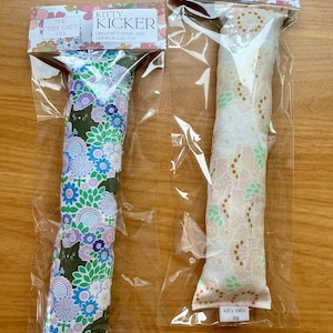 May include: Two cat toys in clear packaging. One has a floral pattern in purple, blue, and green, the other a cream floral design. Each is labelled "Kitty Kicker" and "Organic Catnip and Crinkle Cat Toy".