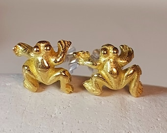 May include: A pair of gold frog earrings. The frogs are facing forward with their legs outstretched. The earrings are made of a shiny metal.