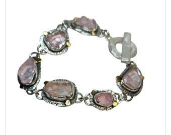 Puede incluir: Una pulsera de plata con piedras preciosas de color rosa claro de forma irregular. Las piedras están engastadas en biseles de plata con detalles dorados y conectadas por eslabones de plata. La pulsera tiene un cierre de palanca.