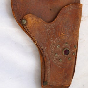 May include: A brown leather holster with a red jewel and the word "RANGER" embossed on the side.
