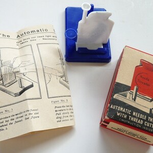May include: A red and white plastic needle threader with a built-in thread cutter. The threader is in a red and white cardboard box with the text "Automatic Needle Threader with Thread Cutter (Instruction Inside)".