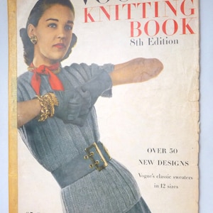 May include: A vintage Vogue Knitting Book cover featuring a woman wearing a gray knitted sweater with a red scarf and black gloves. The cover text reads "Vogue's Knitting Book 8th Edition" and "Over 50 New Designs Vogue's classic sweaters in 12 sizes".