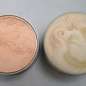 Peut inclure: Un compact rond blanc avec un motif de plumes sur le dessus. Le fond du compact est ouvert, r&eacute;v&eacute;lant une poudre de couleur p&ecirc;che clair.