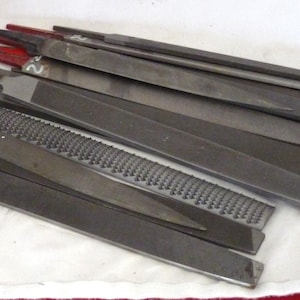 May include: A collection of metal files with different grit sizes. The files are arranged in a pile on a white surface. The files are labeled with the number "2".