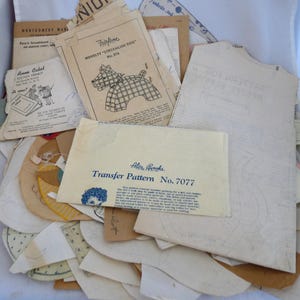 May include: A collection of vintage sewing patterns and ephemera. Includes patterns for a dog, a transfer pattern, and other designs. The papers are aged with visible wear and tear, showing their history.
