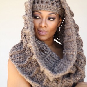 May include: A brown crocheted cowl with a matching crocheted hat. The cowl is thick and has a loose, drapey fit. The hat is a beanie style with a wide brim.