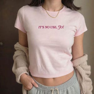 May include: Pink cropped t-shirt with the text "IT'S NO USE, Jo!" in burgundy lettering.