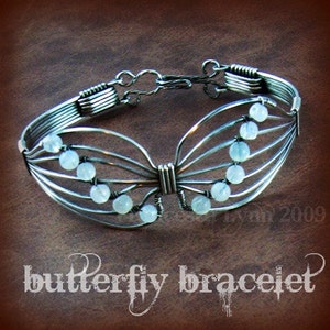 May include: A silver-toned butterfly bracelet with pale blue beads. The bracelet is made of wire and has a delicate, open design. The text "butterfly bracelet" is at the bottom of the image.