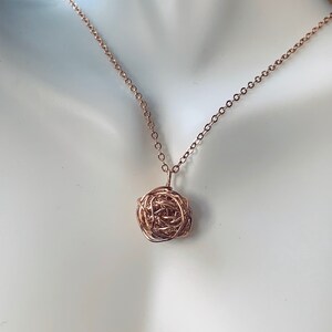 May include: A rose gold necklace with a delicate, intricate pendant made of twisted wire.